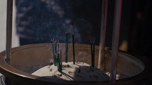 Incense sticks burning and smoking in a sand filled bronze censer at a Buddhist temple in Japan
