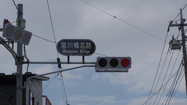 Miyagawa Bridge intersection sign with Japanese traffic lights and tangled power lines under a cloudy sky in Japan