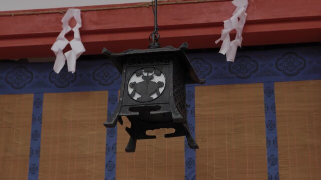 Ornate cast metal hanging lantern with white shide streamers and blue curtain at a Japanese Shinto shrine
