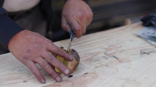 Hands slicing a roasted sweet potato with a knife on a rustic wooden board in soft outdoor light
