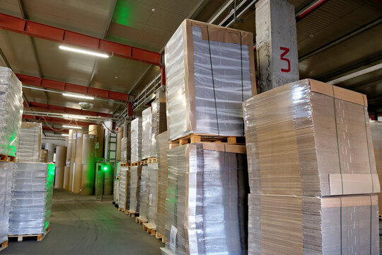 High stacks of cardboard material on wooden pallets stored in a spacious logistics warehouse facility