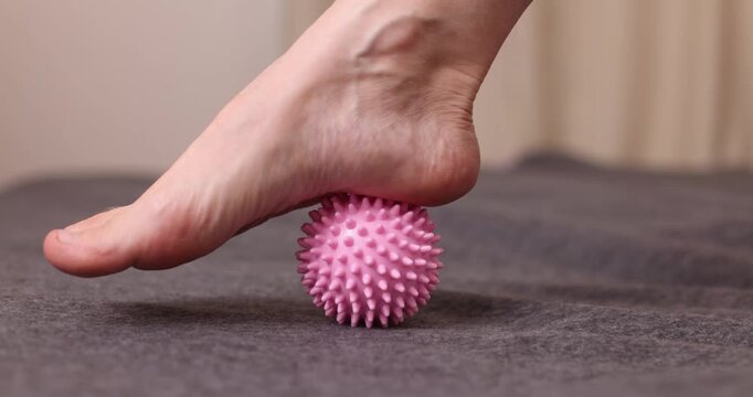 Foot pressing a pink spiky ball on a dark surface, close-up of a tactile moment, simple object interaction, indoor activity, casual scene.
