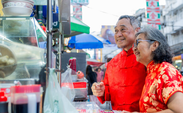 Elderly couple enjoying street food at a market in the evening with colorful lights in the background