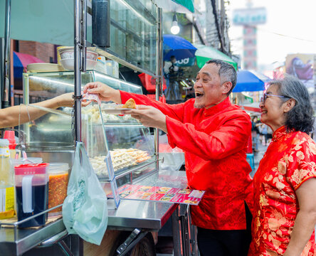 People enjoying food at a street vendor in a busy market during the daytime in an urban setting