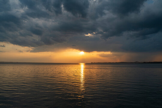Dramatic sunset over Lake Constance seen from the Austrian shore in Bregenz, Vorarlberg, with the golden sun breaking through dark storm clouds and reflecting on the calm water surface