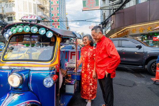 Couple stands beside a tuk-tuk in a city street during a festival celebration in the late afternoon