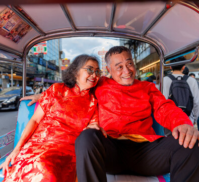 Elderly couple enjoys a ride in a tuk-tuk while wearing traditional red outfits in a busy street