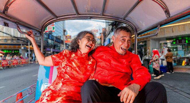 Elderly couple enjoys a ride in a tuk-tuk during a festive event in a busy street at dusk
