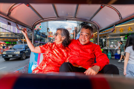 Couple wearing red traditional outfits enjoying a tuk-tuk ride in a busy market street at night
