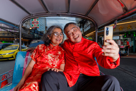 Couple takes a selfie while sitting in a tuk-tuk in a busy street during the evening