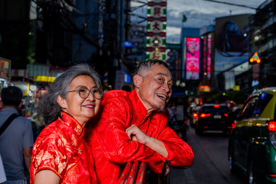 Couple in traditional outfits smiles on a busy street during the evening in a city with bright signs