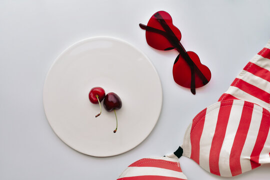 Cherries on a plate, red sunglasses and red striped swimsuit on white background