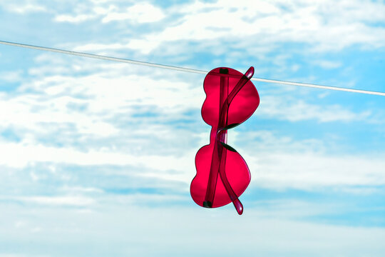 Red heart-shaped sunglasses on clothesline against a blue sky