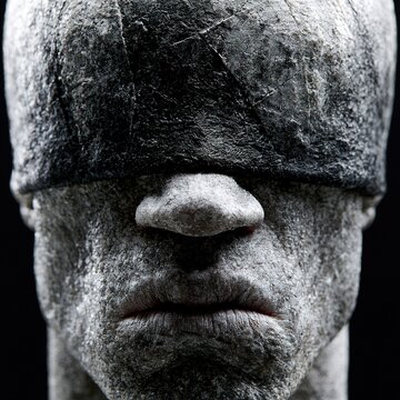Stone head statue blindfolded in darkness symbolizing ignorance