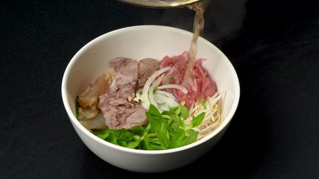 Pouring hot flavorful beef broth into a bowl of traditional Vietnamese Pho.