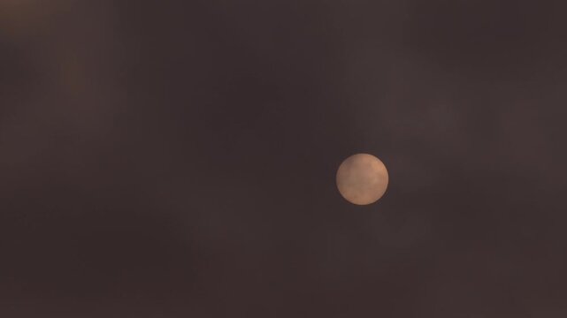 Detailed View of the Sun Disk with Visible Sunspots, Naturally Filtered by Clouds in the Sky.