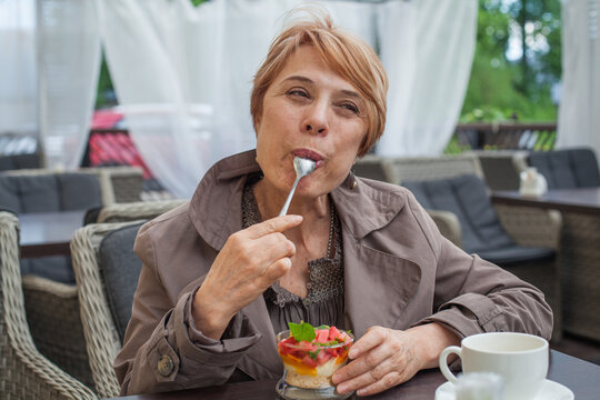 Elderly woman enjoys dessert in cafe during afternoon with warm light and relaxed environment in the background