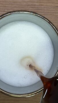 Barista pouring espresso into milk foam making latte