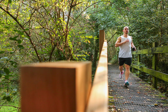 A young man running in nature, crossing a wooden bridge between trees.