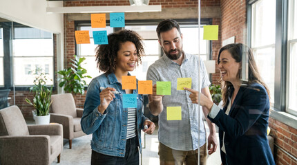Obraz premium Creative professionals collaborate around glass whiteboard with colorful sticky notes, brainstorming ideas during startup meeting in modern office with natural daylight and copy space.