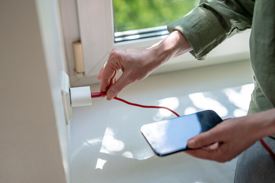 Woman connecting damaged phone charger cable trying to recharge smartphone, plugging in outlet on wall, issues with mobile charge due to kinked charging wire, female connecting cellphone power cable