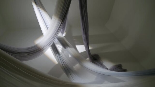 Suspended pleated fabric installation with crossed loops, sweeping drapes, layered folds, and soft directional light inside minimal contemporary interior, with fabric, drape, pleated, sheer detail