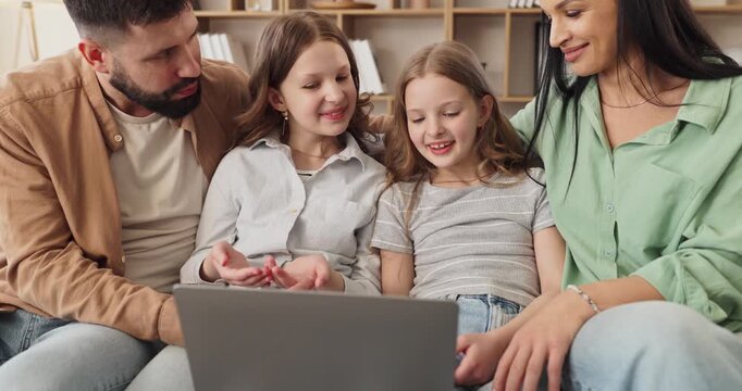Family parents children video call online laptop home. They sit on a couch smiling at the screen, waving and chatting with relatives in a warm room. Concise family communication concept today.