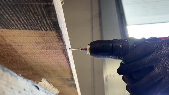 Worker using cordless screwdriver to drill screw into wood