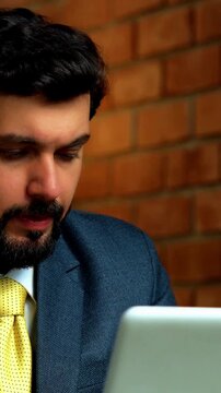 Working on laptop and thinking deeply, Indian businessman imagines future while gazing out of office window during break, wearing formal attire in cozy corporate workspace with terracotta brick wall