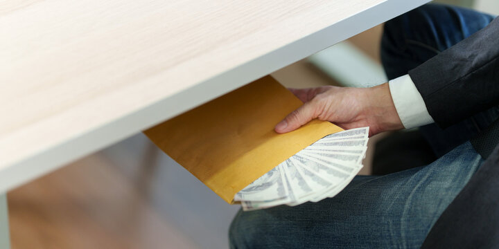 Cropped hand passing envelope with money under desk for bribery concept