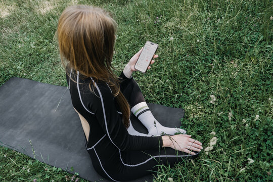 Woman sitting outdoors holding smartphone displaying fitness dashboard with heart rate and calorie metrics. AI fitness tracker data, smartwatch monitoring, biohacking lifestyle, urban wellness, heart