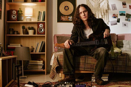 Portrait of young adult Caucasian man holding electric guitar at home, presenting independent music creation and artist branding. Useful for music marketing, streaming promotion