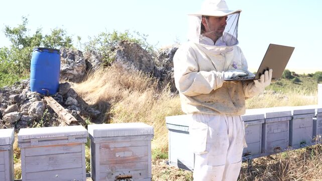Beekeeper using a laptop computer to manage hives and honey production at a rural apiary