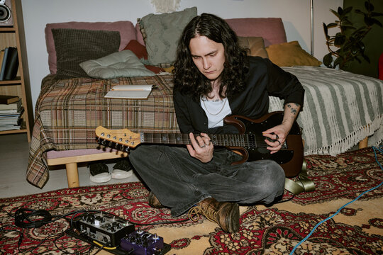 Young adult Caucasian man playing electric guitar at home, practicing music production and songwriting. Useful for indie artist branding, home studio, creative lifestyle marketing