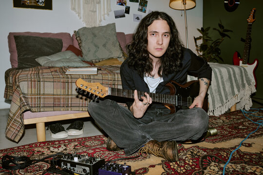 Portrait of young adult Caucasian man playing electric guitar at home, creating rock music content. Ideal for music lifestyle marketing, home studio promotion, medium shot