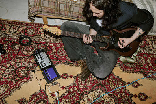 Overhead of young adult man playing electric guitar at home, practicing riffs with pedalboard and cables, expressing independent music creation. Useful for home studio, musician lifestyle marketing