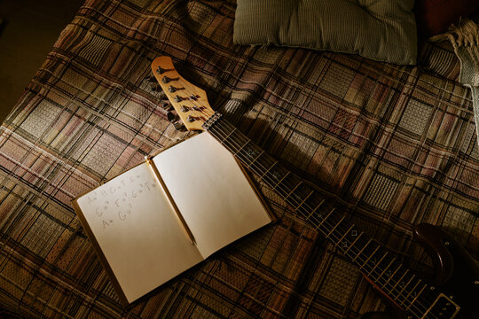 Overhead shot of electric guitar and notebook showing chord notes on bed, supporting songwriting and home music practice. Useful for music education, creative process, artist branding