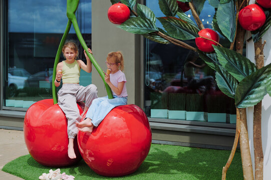 Girls enjoying a unique cherry-themed play area with oversized fruit sculptures