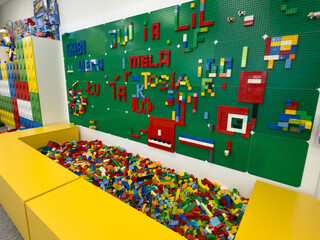 Obraz premium Colorful lego bricks in a yellow bin with a green brick wall in a children's play area, showing a creative building and toy activity space