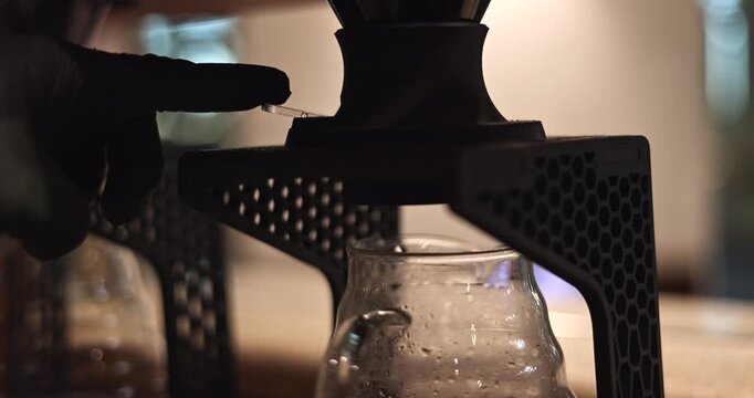 Fresh brewed coffee drips into a glass server beneath an automated pour over brewer, hands push button release, slow motion