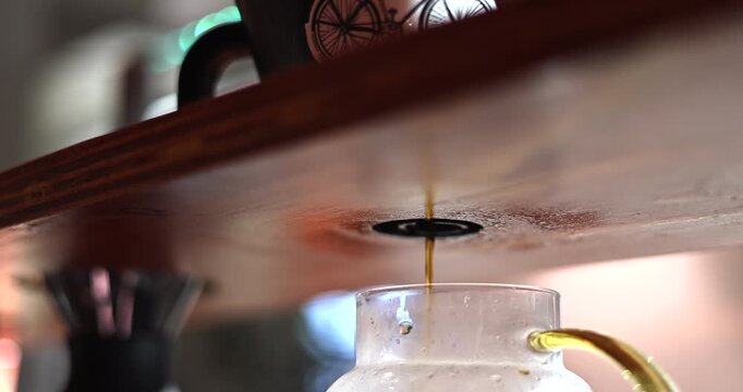 Fresh brewed coffee streams from the brewer into a textured glass server beneath wooden counter, slow motion drip