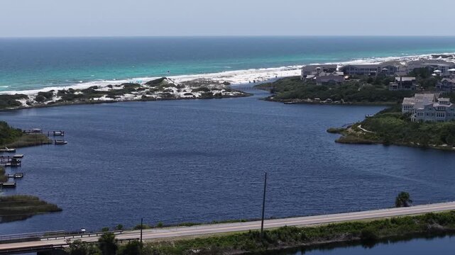 Dynamic perspective drone shot of Camp Creek Lake environment with emerald Gulf and 30A Highway running across lakeside community, Florida, US