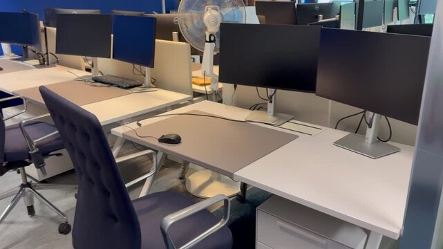 An empty modern office featuring multiple computer monitors ergonomic chairs and clean minimalist desks
