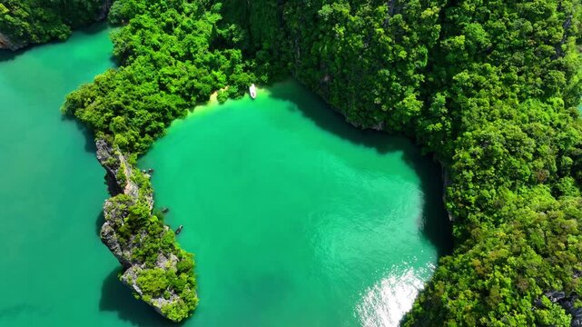 A small boat parked in turquoise waters surrounded by limestone karst formations covered in dense tropical vegetation at Ao Phang Nga National Park. Ku Du Yai Island Phuket Thailand.