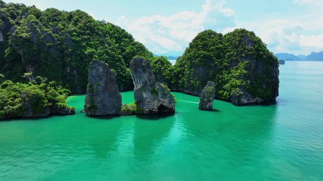 Longtail boat navigates through turquoise waters between limestone karst islands at Ao Phang Nga National Park near Phuket, Thailand. Smooth pull out aerial tracking shot Ku Du Yai Island ocean safari