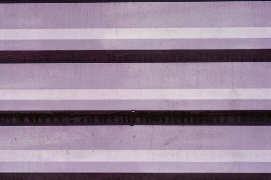 A detailed close up horizontal shot captures the linear textured pattern of a corrugated purple metal panel with horizontal ridges and distinct parallel shadows