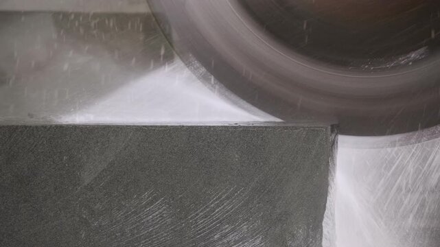 Industrial circular saw cutting block of stone with water cooling in a factory, close up