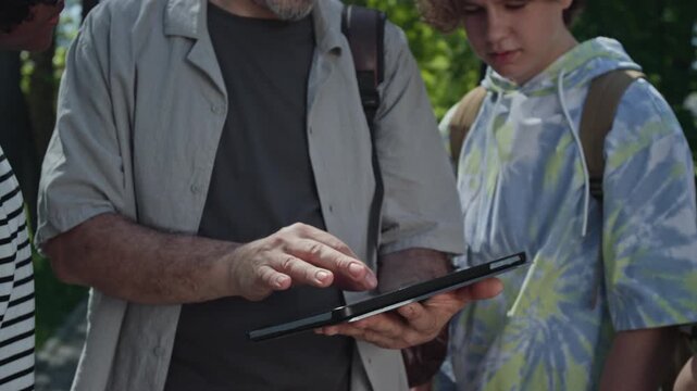 Middle aged man showing educational content on tablet to teenagers outdoors. Clip for promoting digital learning platforms and modern school curricula