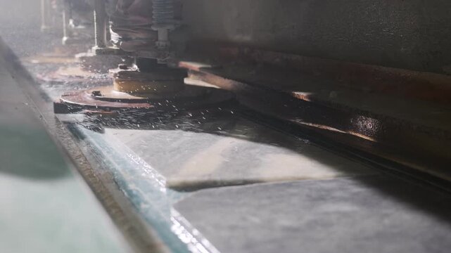Industrial machine polishing marble slab surface with water in a factory workshop