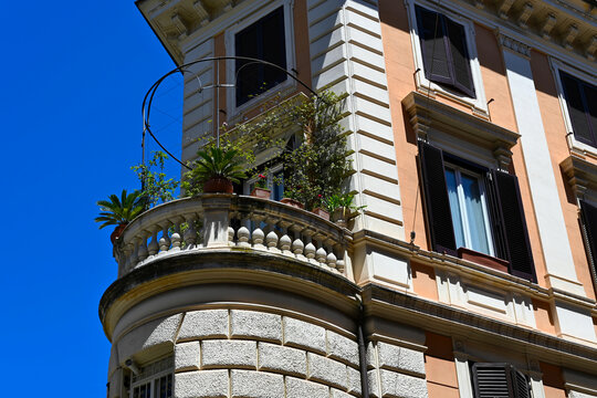 classic old circular stone balcony. stone balustrade and railing and sill. flowers in flower pots. concrete slab.  decorative stucco exterior elevation. wood windows and shutters